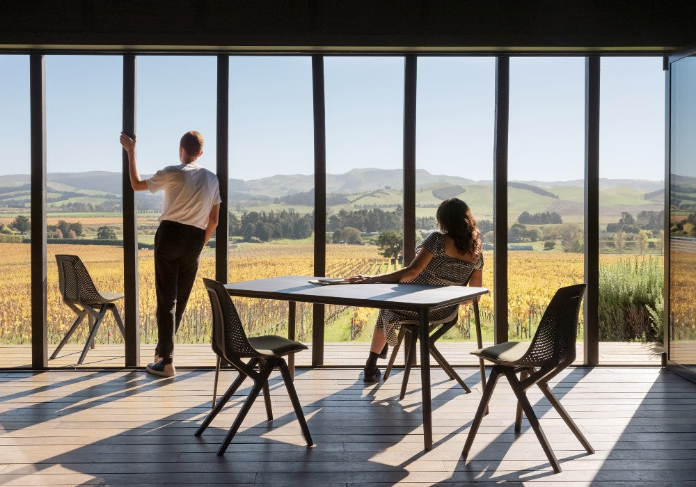 Two people in their living room admiring the view, with black Noho chairs made with ECONYL® regenerated nylon in the background.