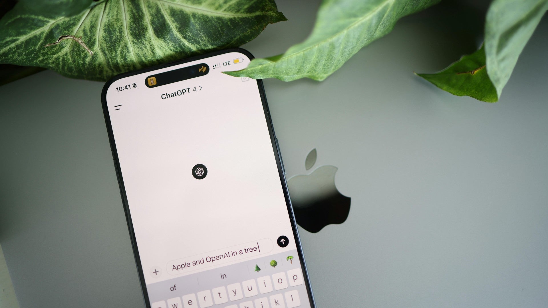 An iPhone showing the ChatGPT app resting on a MacBook next to green leaves.