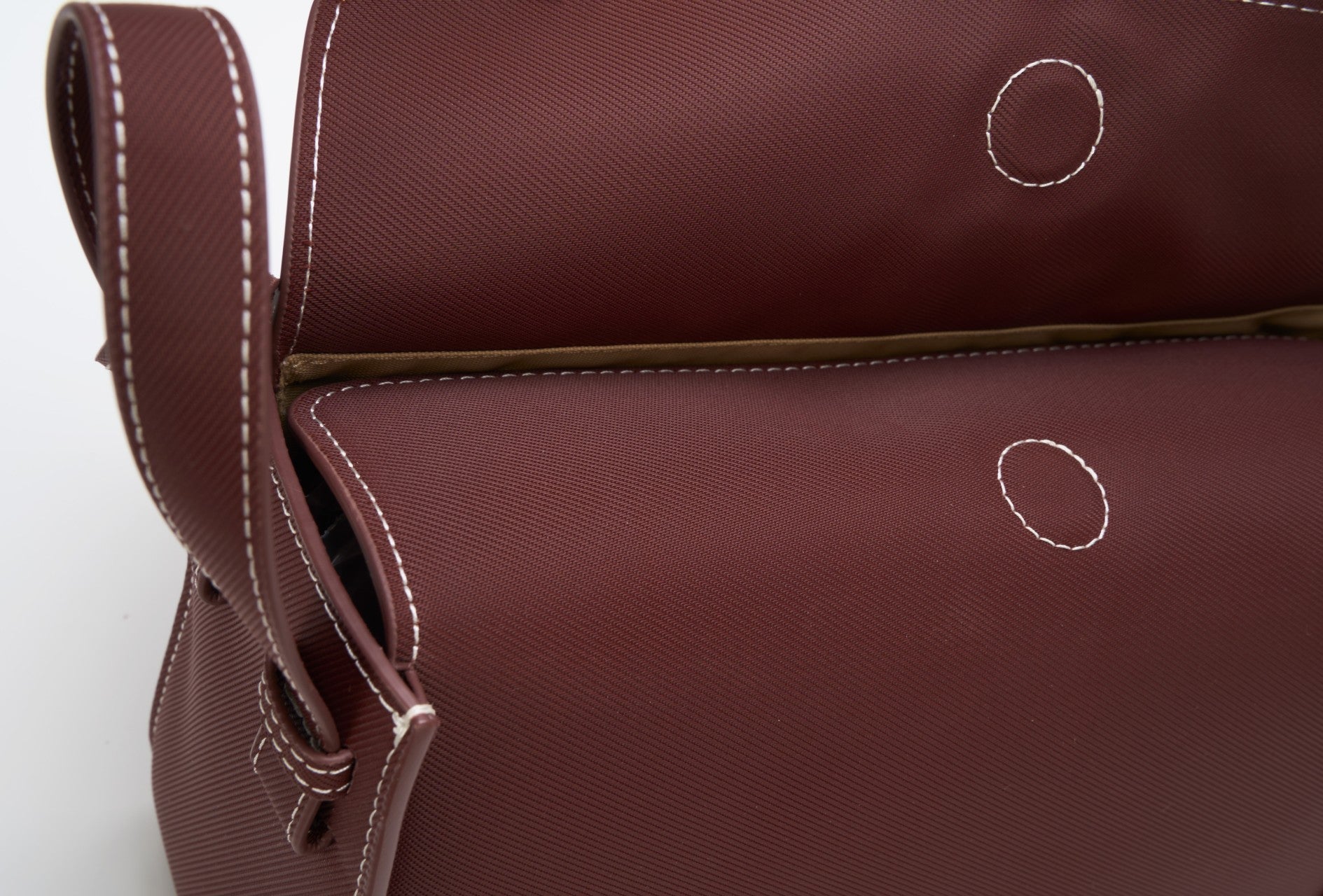Close-up of a brown bag, made with ECONYL® regenerated nylon, with white stitching on a white background