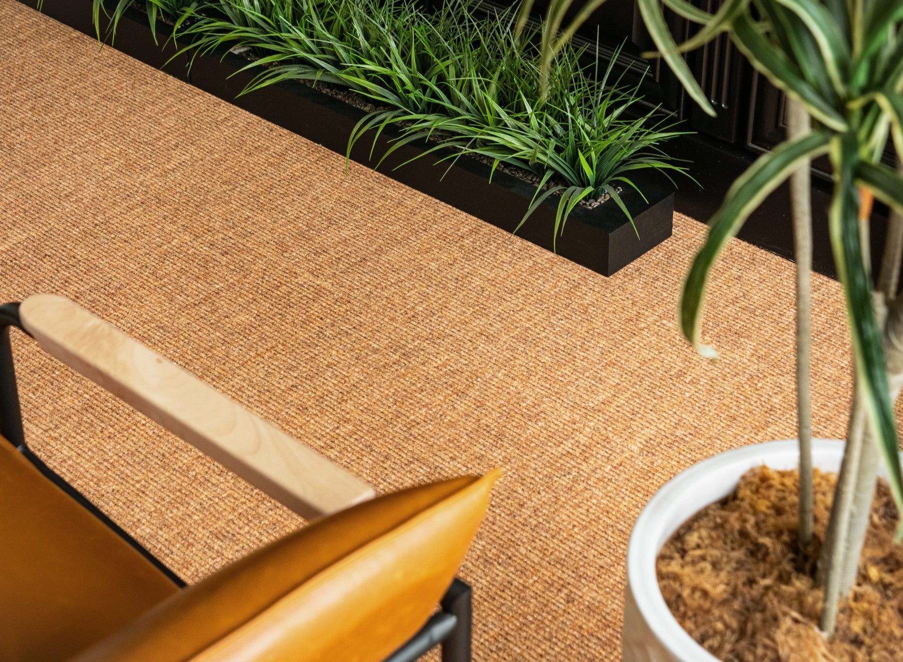 Brown woven surface with a chair and potted plant. Rug by Synsisal made with ECONYL® regenerated nylon