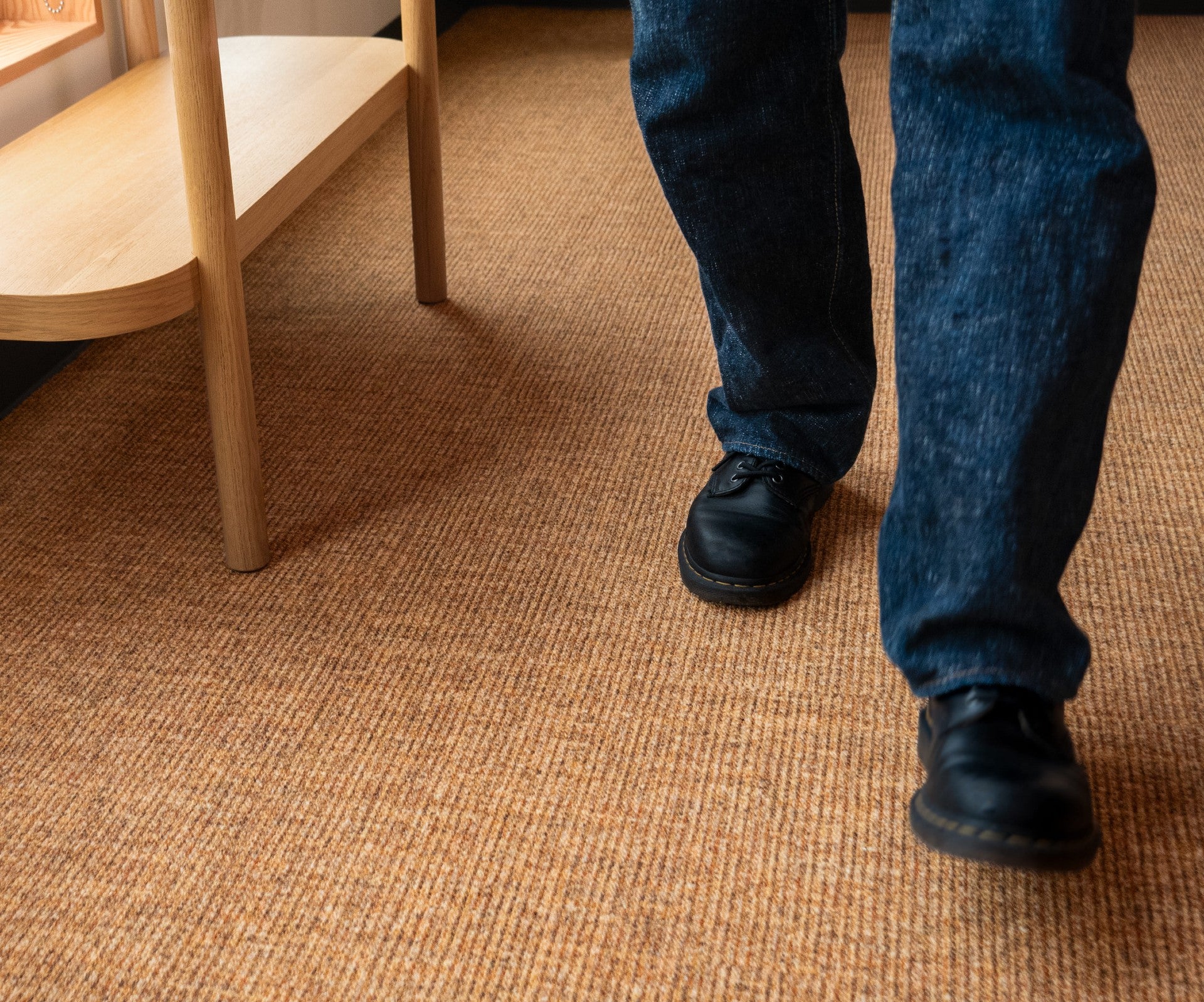 Person wearing blue jeans and black shoes on a brown carpet. Rug by Synsisal made with ECONYL® regenerated nylon