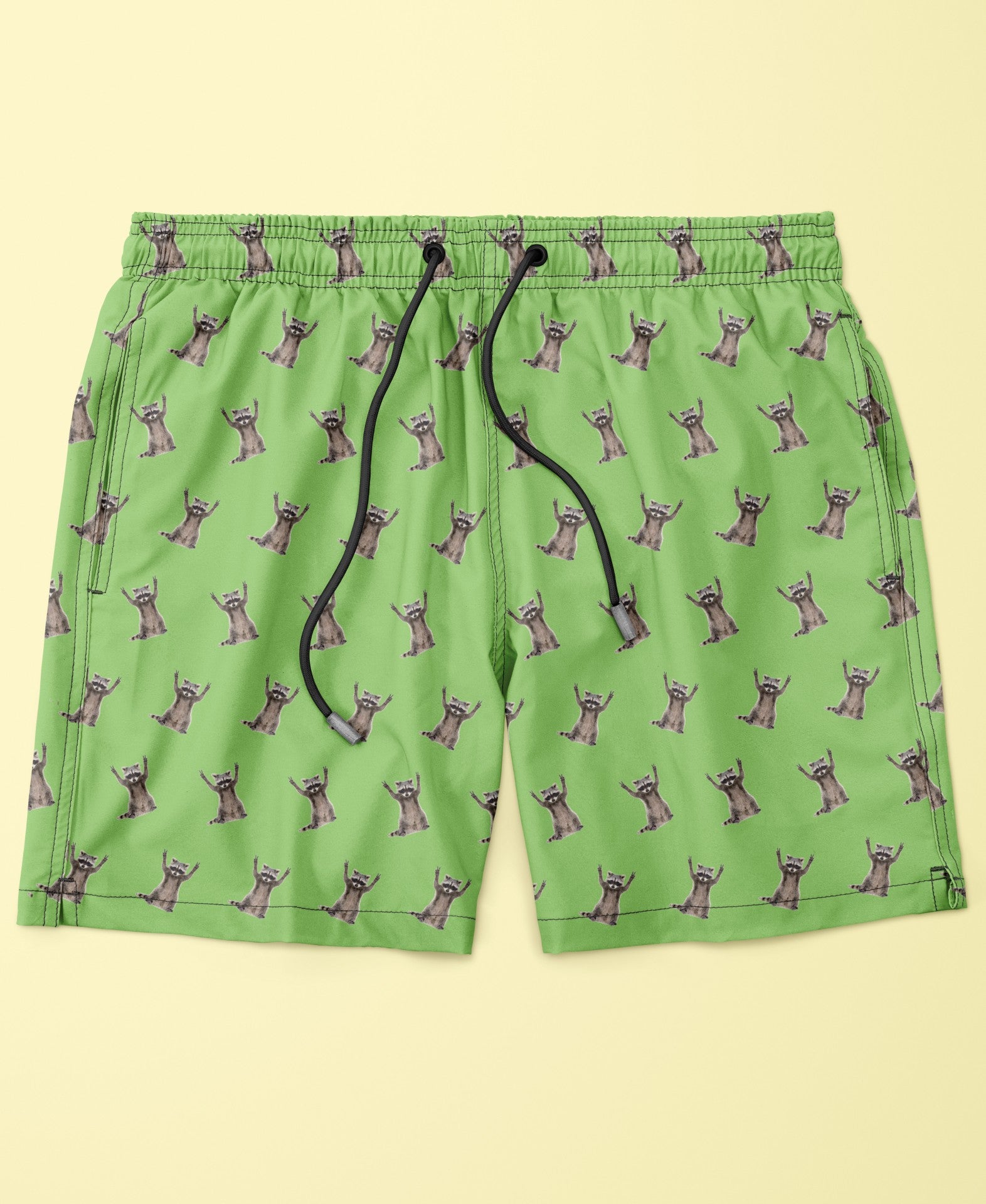 Green swim shorts made with econyl nylon with raccoon pattern on a beige background