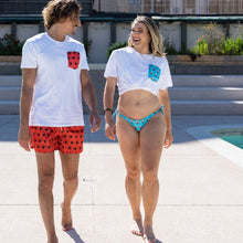 Load image into Gallery viewer, Two people walking by a pool with a cityscape in the background
Their swimsuits are made with econyl nylon
