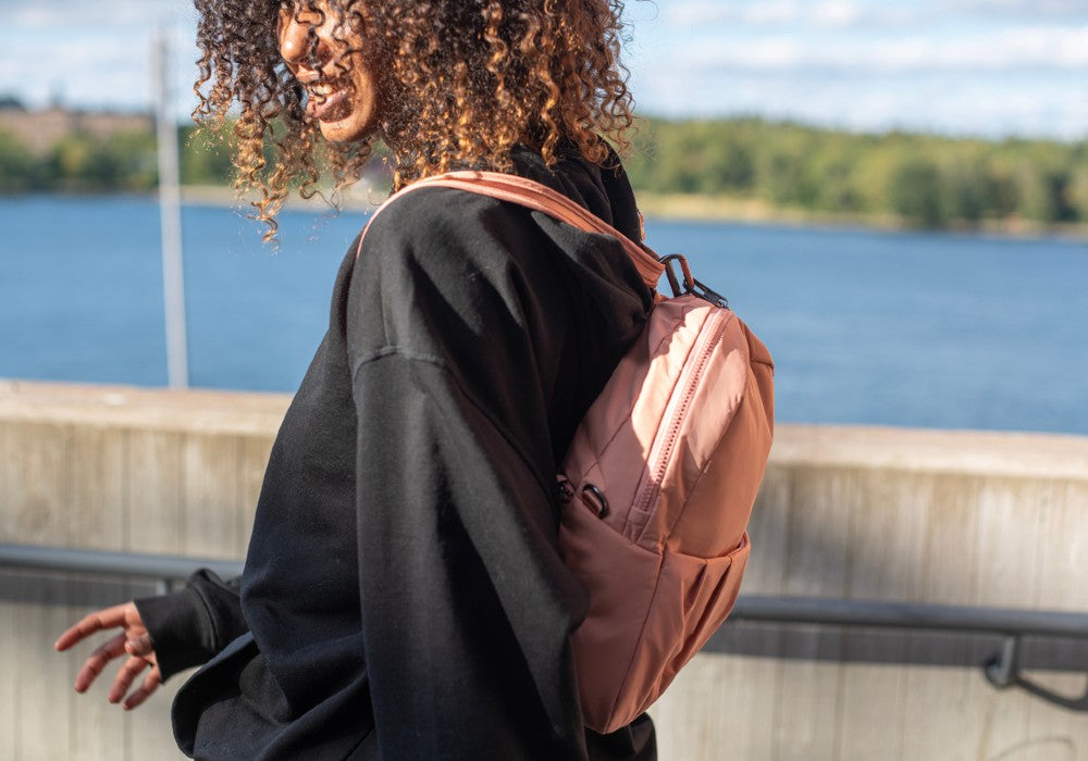 Woman walking with the Pacsafe Citysafe CX Anti-Theft Convertible Backpack color Rose made with ECONYL® regenerated nylon