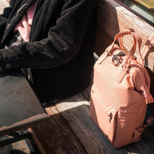 Load image into Gallery viewer, Woman sitting with the Pacsafe Citysafe CX Anti-Theft Mini Backpack color Rose made with ECONYL® regenerated nylon
